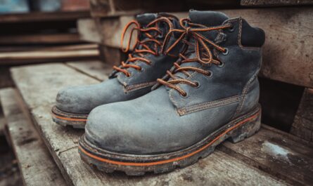 Par iznošenih radnih čizama od kože sa narandžastim pertlama na drvenoj podlozi